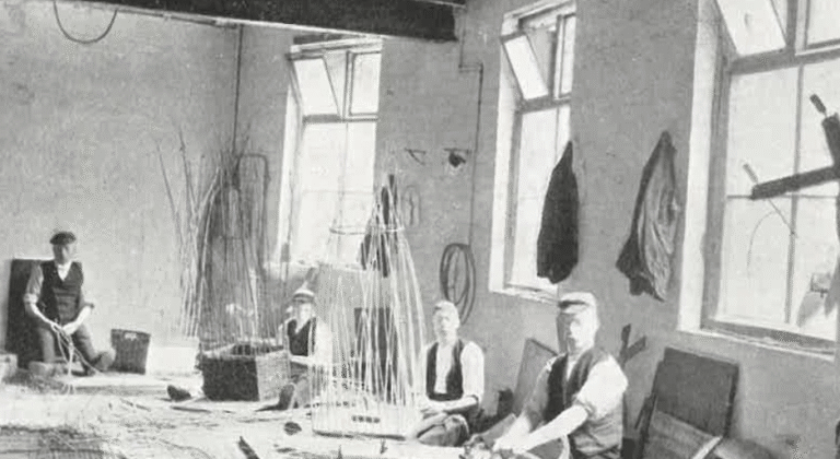 This image shows an old photo from Beacon's archives of men in Victorian times making wicket baskets in a large warehouse space.