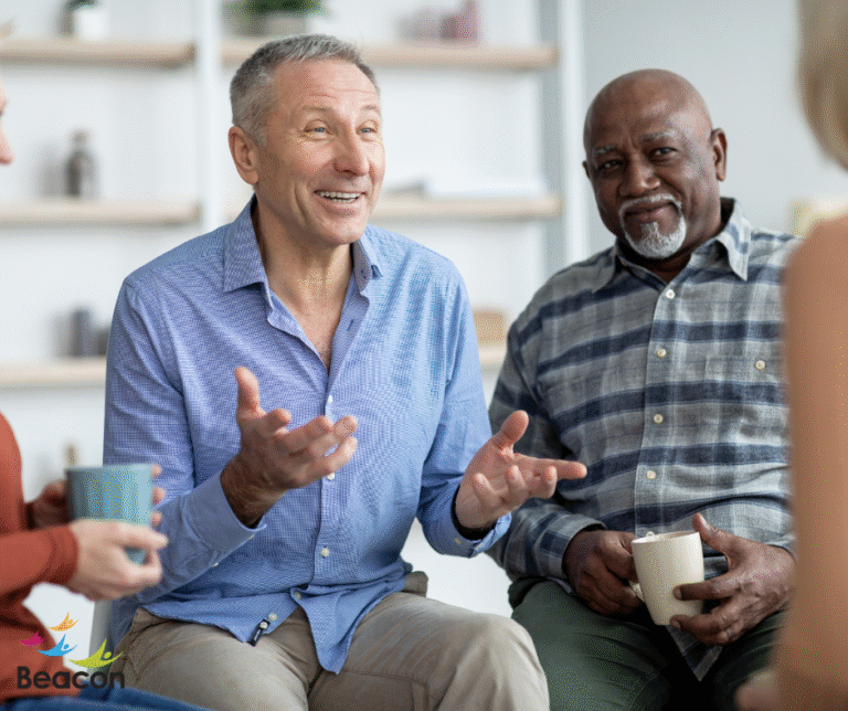 This shows a group of older people talking, two men can be seen in full, one man is gesturing and laughing as he talks.